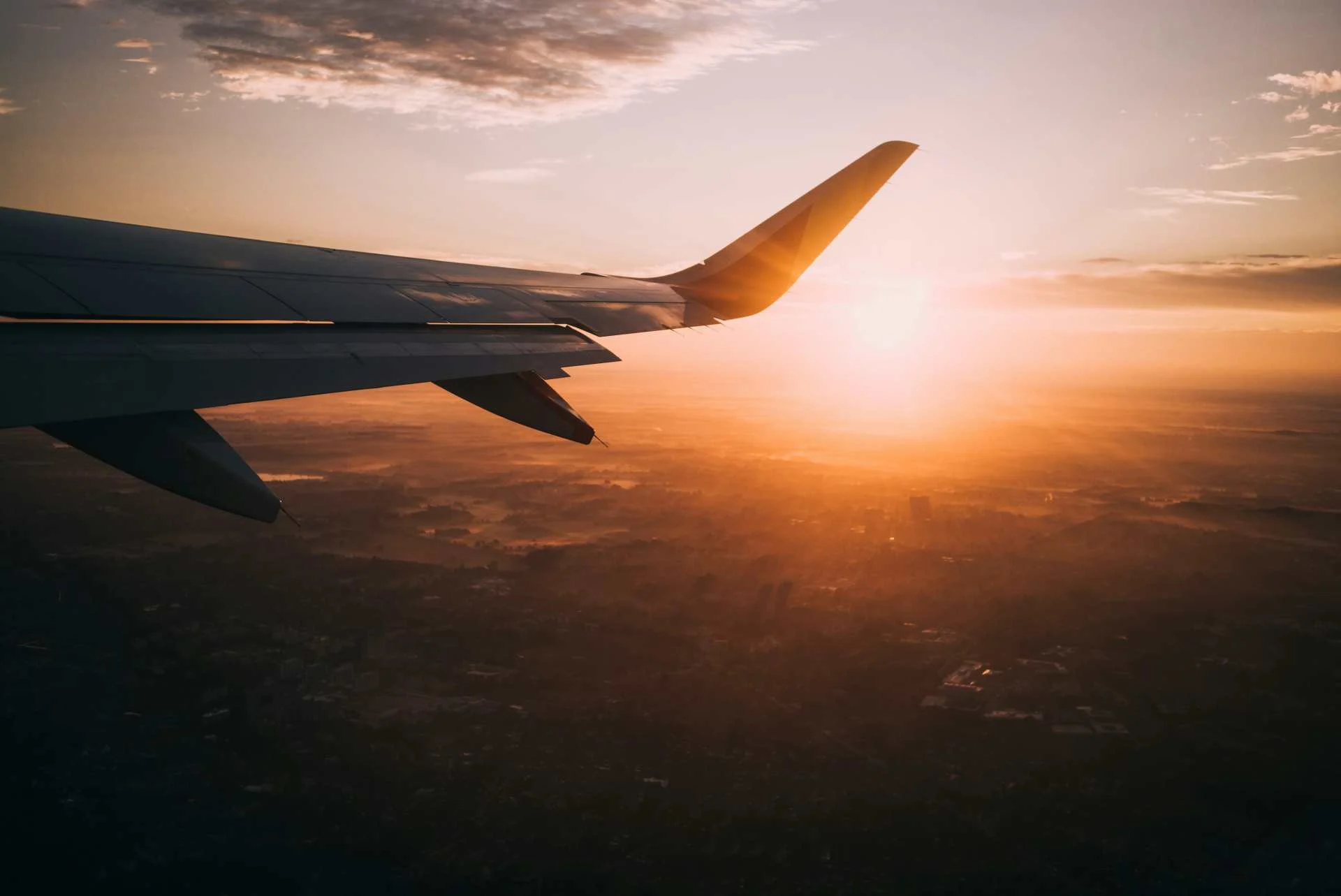 Aerial view from a plane window of a wing silhouetted against orange sunset clouds, illustrating the point.me monthly roundup of credit card and airline loyalty transfer bonuses.