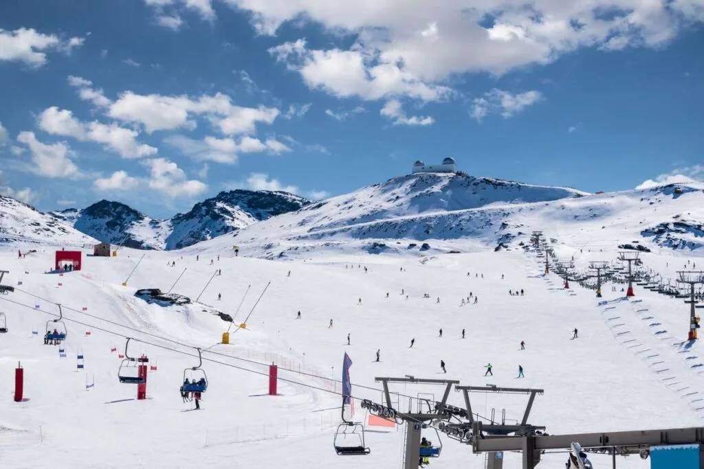 Skiers and chairlifts on the slopes of Spain's Sierra Nevada ski resort, with an observatory perched on the peak above