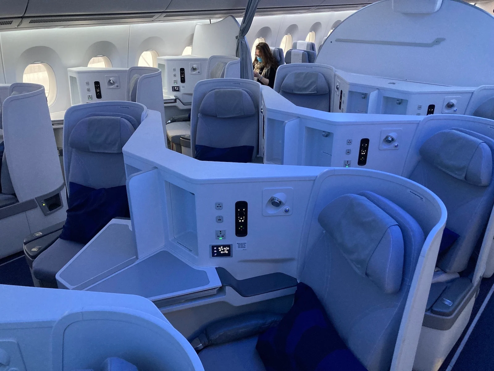 Finnair Airbus A350 business class cabin with staggered herringbone seats in blue and white, and a flight attendant standing near the front.