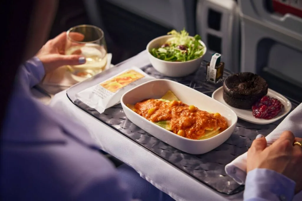 Delta Premium Select meal service with a glass of white wine, side salad, pasta entree, and chocolate dessert on a tray table
