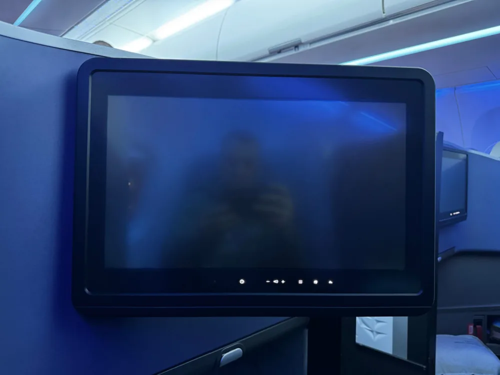 Blank JetBlue Mint seatback entertainment screen showing a passenger's reflection while photographing it