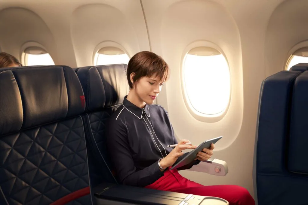 A woman in Delta's premium cabin using a tablet in a window seat with dark leather seating