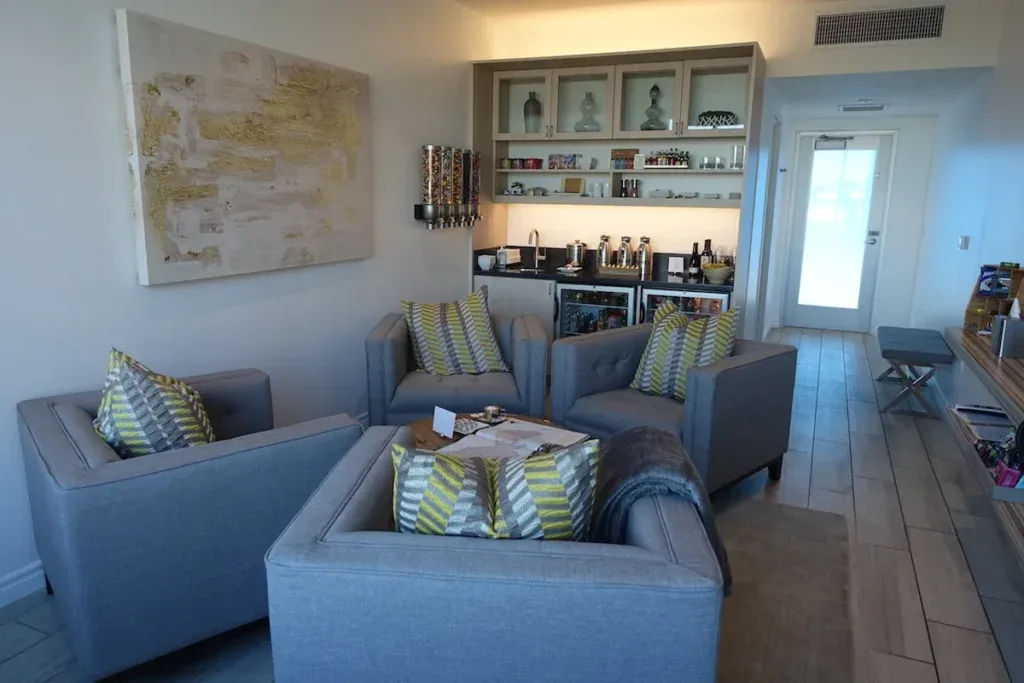 A private lounge suite at The Private Suite LAX, with gray armchairs, artwork, and a stocked mini-bar area