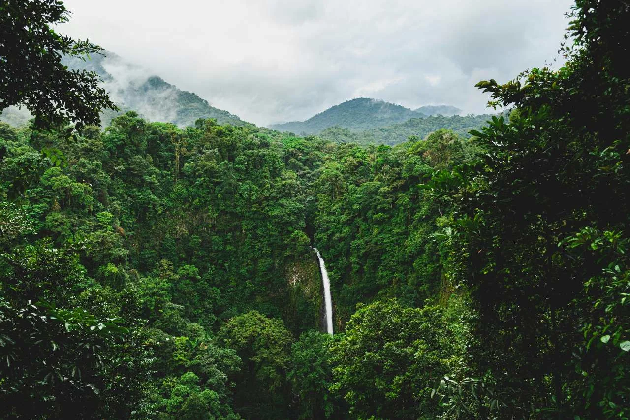 A waterfall cascading through a lush green rainforest gorge in Costa Rica, with misty mountains in the background