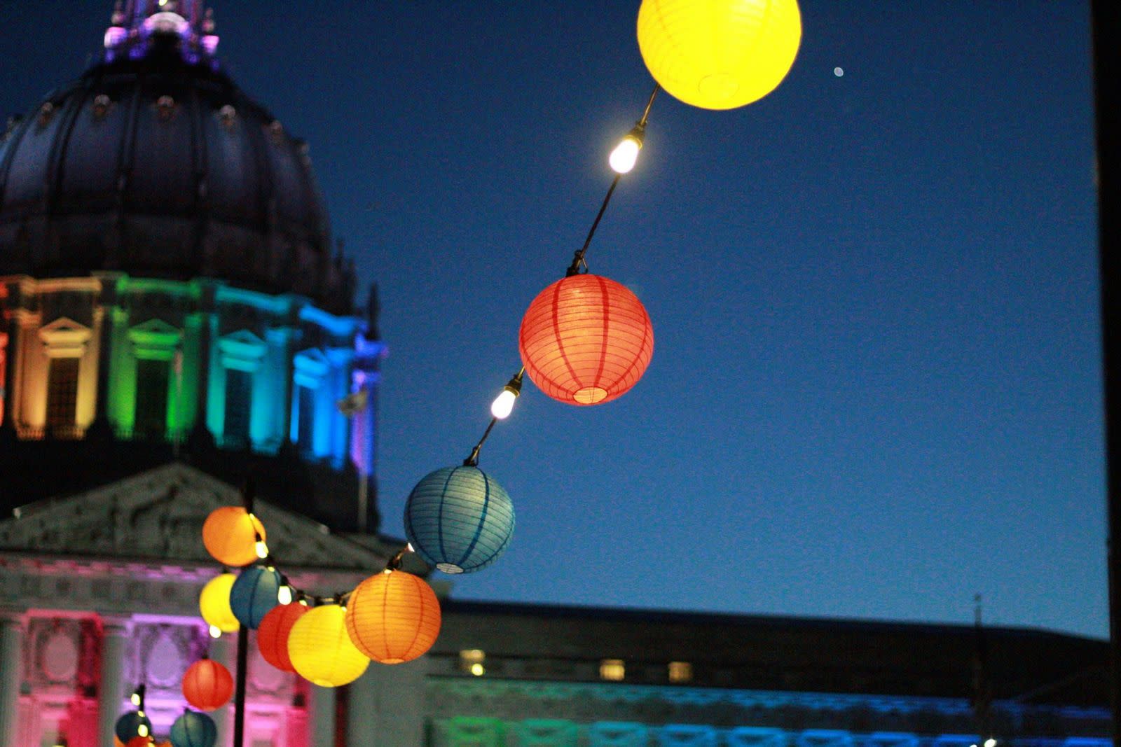 San Francisco City Hall lit in rainbow colors at dusk, with colorful paper lanterns strung across the plaza. San Francisco City Hall lit in rainbow colors at dusk with strings of paper lanterns, marking SF Pride — one of the largest queer celebrations in the U.S.