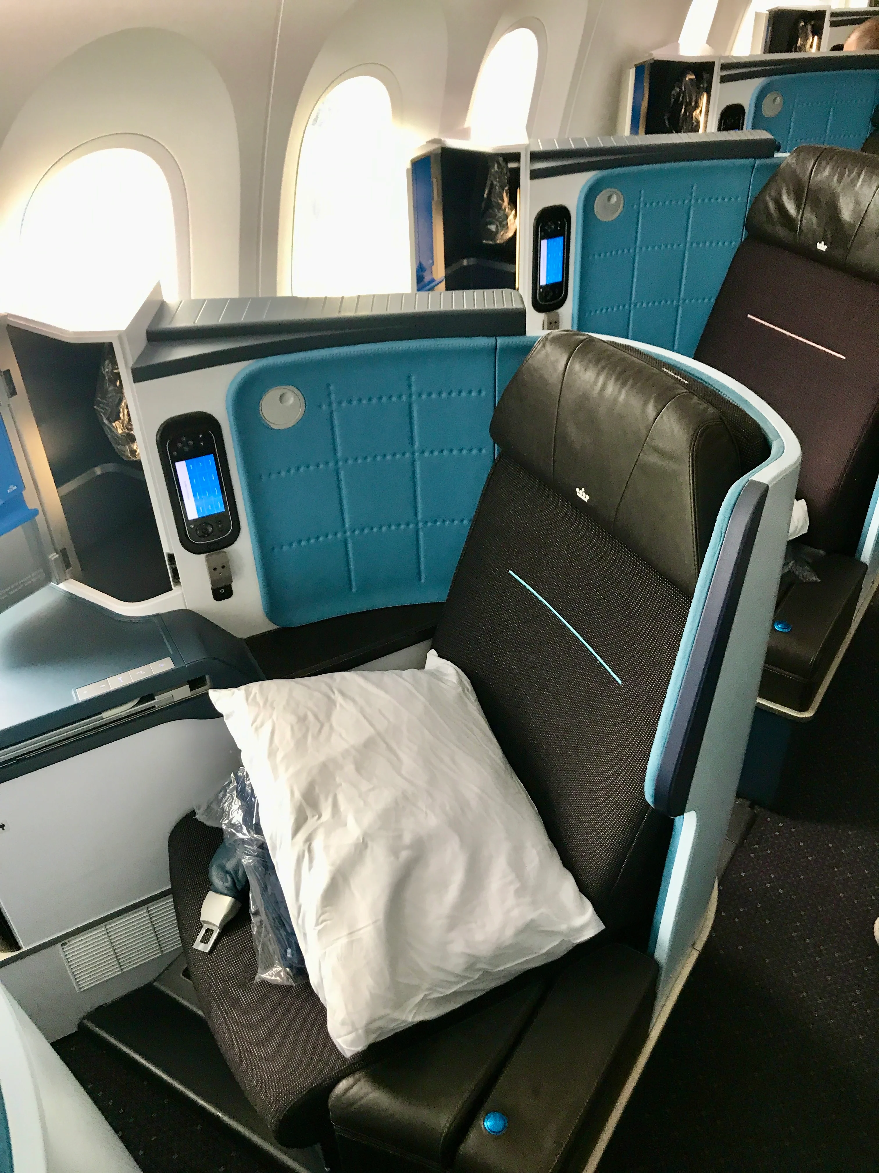 KLM business class seat with teal accents, a personal entertainment screen, and a pillow placed on the footrest