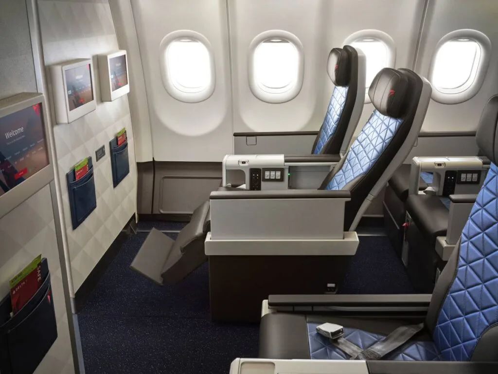 Delta Premium Select cabin showing blue diamond-quilted recliner seats with adjustable footrests and a seatback welcome screen