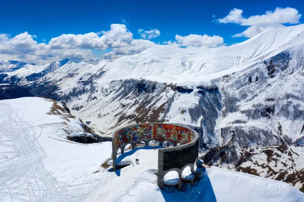 The circular Soviet-era Friendship of the Peoples monument overlooking snow-covered mountains at Gudauri ski resort in Georgia
