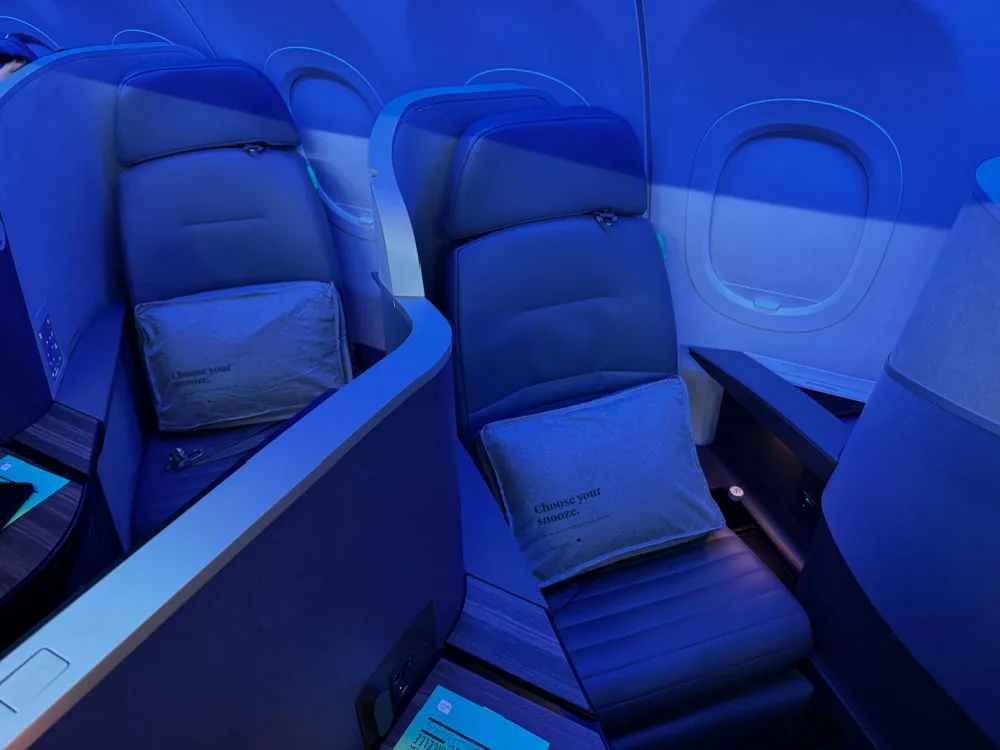 Two JetBlue Mint suites side by side with pillows and privacy dividers, lit in blue during a night flight