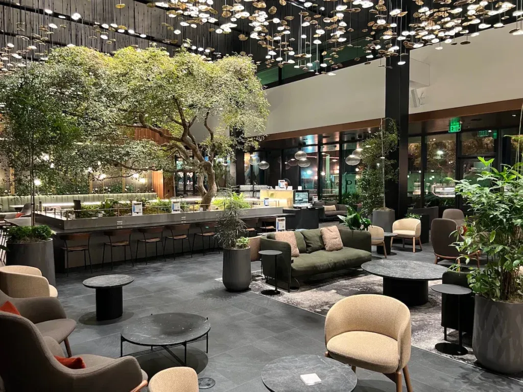 Lounge seating area at the Amex Centurion Lounge in Atlanta, centered around a large indoor tree beneath a canopy of hanging lights