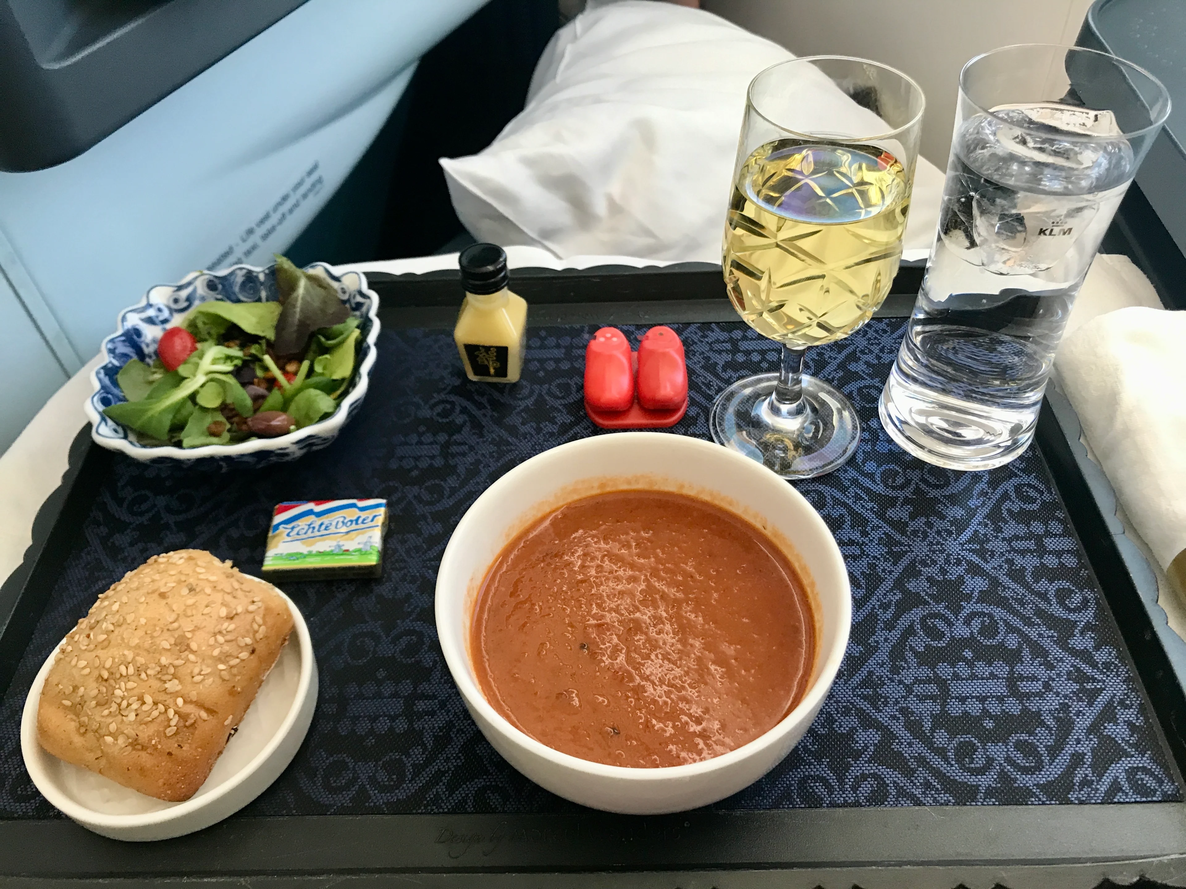KLM in-flight meal service with a side salad, tomato soup, bread roll, and a glass of white wine on the tray table