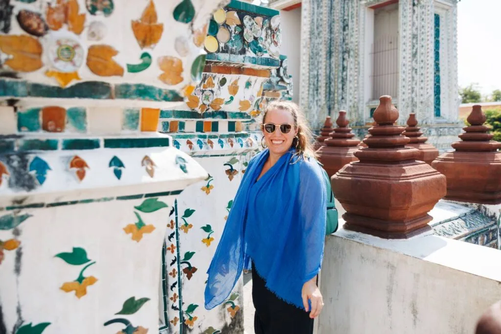 A traveler in a blue scarf smiling in front of an ornately tiled Buddhist temple in Thailand