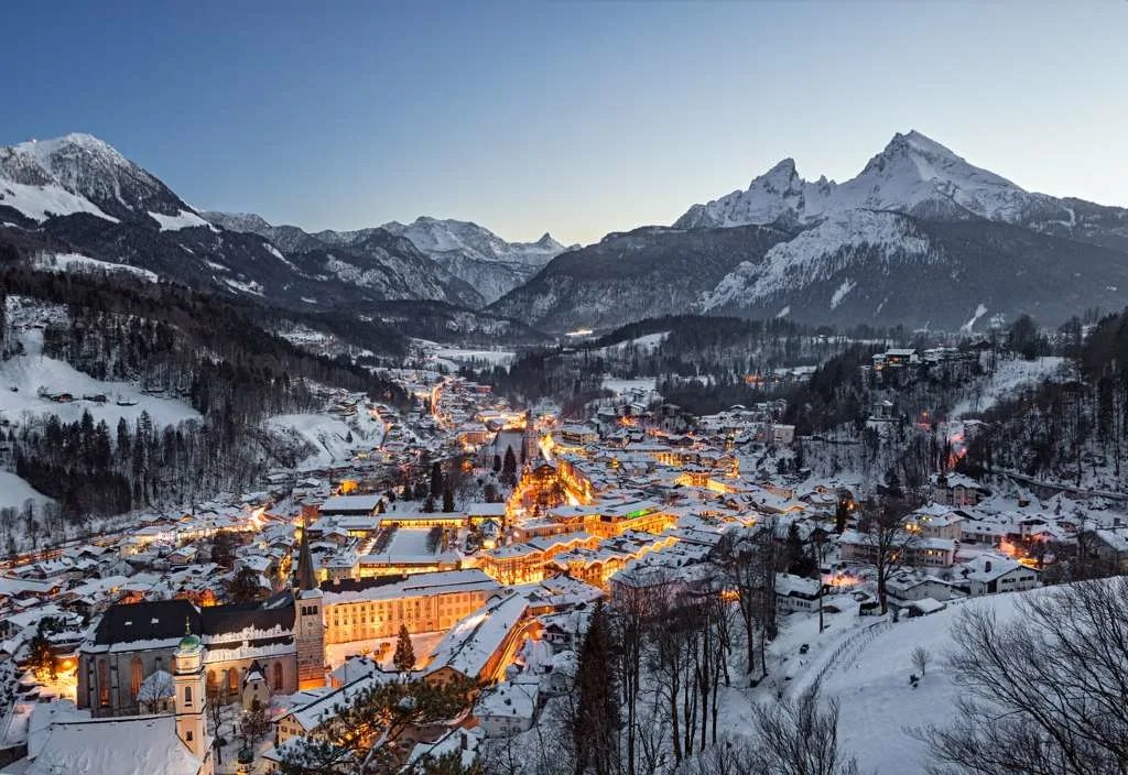 The snow-covered town of Berchtesgaden, Germany, illuminated at dusk beneath the jagged Watzmann mountain range