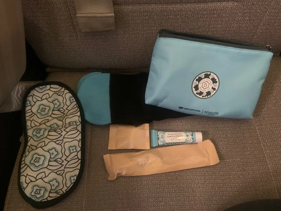 TAP Air Portugal business class amenity kit contents including a floral sleep mask, socks, lip balm, and a toiletry pouch laid out on a seat.