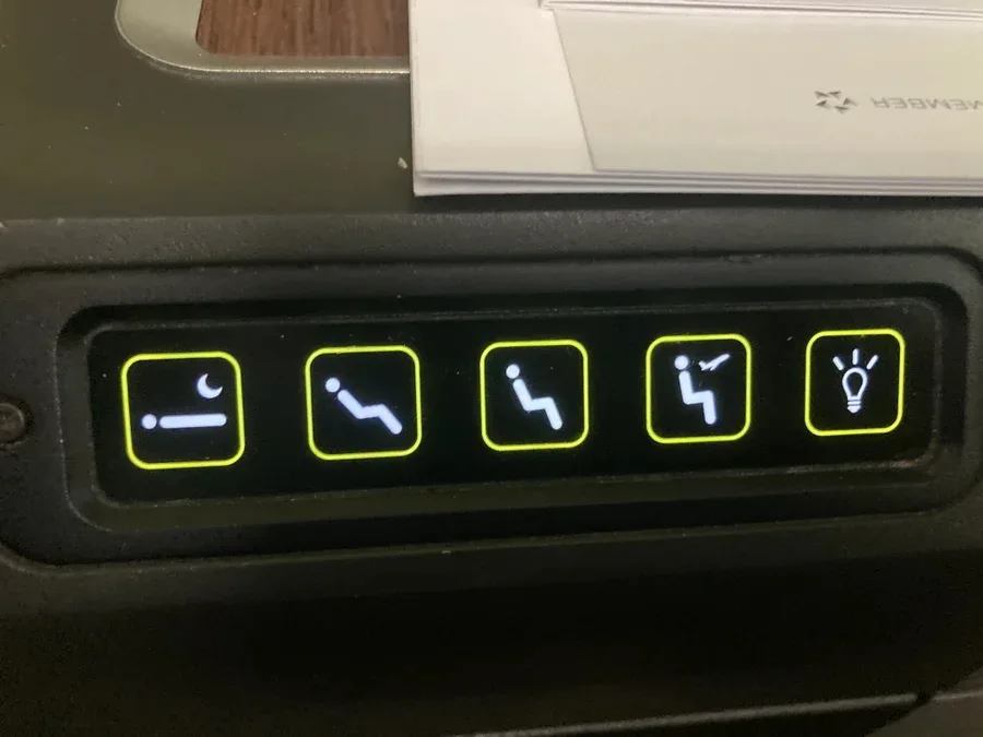 Close-up of illuminated seat control buttons on a TAP Air Portugal business class seat, including recline, footrest, and light functions.