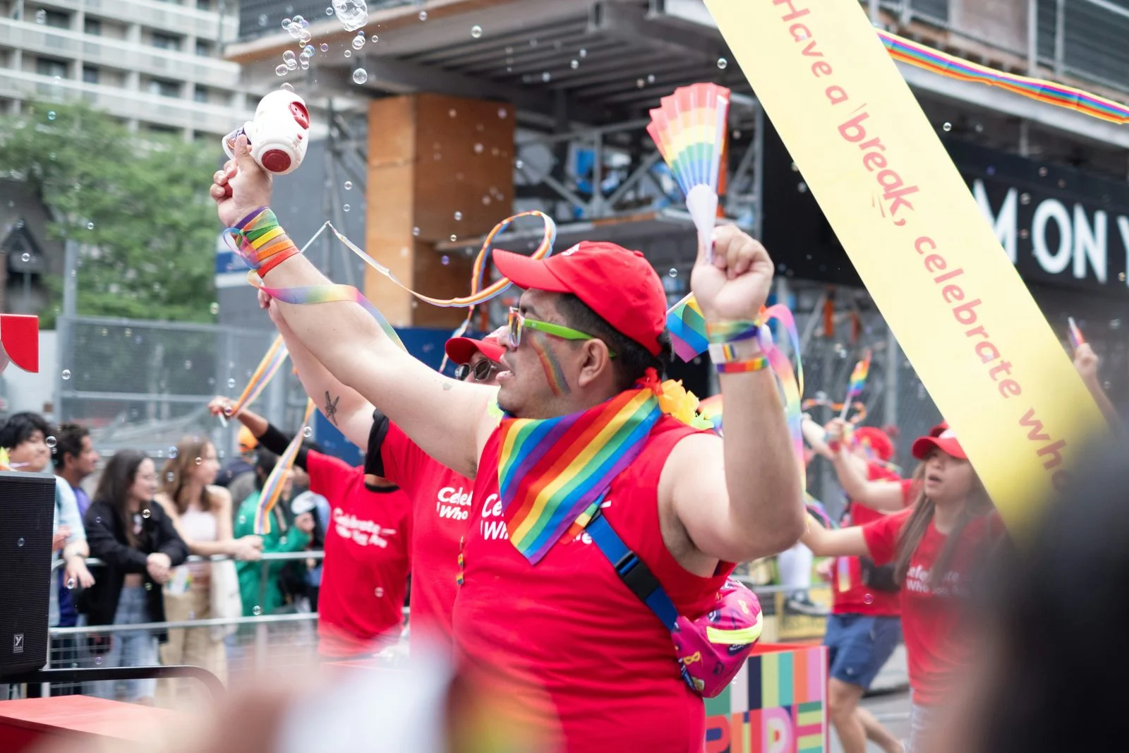 Performer on a Toronto Pride parade float sprays foam and holds a rainbow fan beneath a sponsor banner. A performer on a Toronto Pride parade float sprays foam and holds a rainbow fan, capturing the joy of Canada's largest Pride celebration.