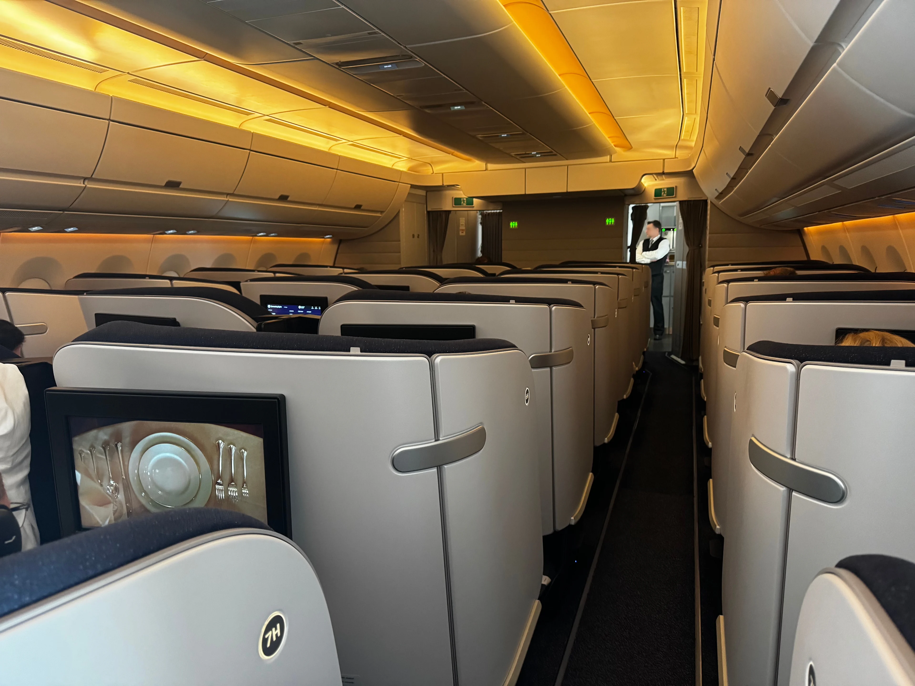 View down a Finnair A350 business class cabin aisle with warm ambient lighting, individual seat pods, and a crew member standing near the cabin divider.
