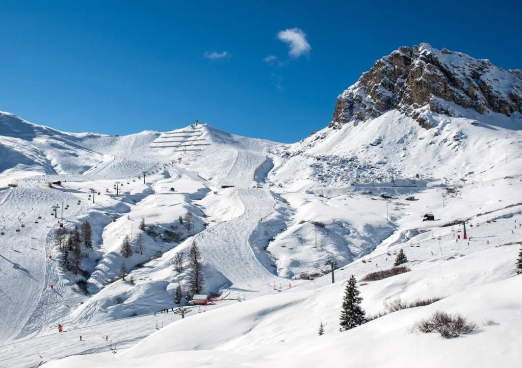 Snow-covered ski slopes and lift lines beneath a rocky mountain peak in the Italian Dolomites