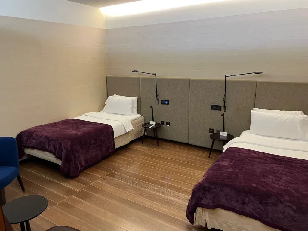 A private rest suite in the Qatar Airways Al Safwa First Lounge in Doha, featuring two beds with plum-colored blankets and reading lamps