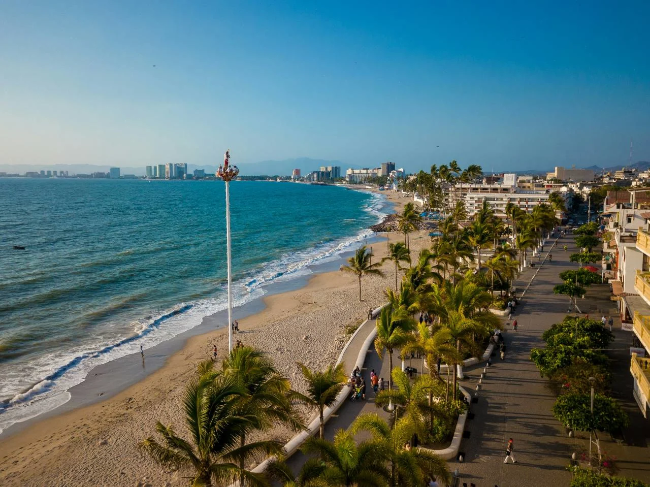 Aerial view of the Puerto Vallarta beachfront boardwalk lined with palm trees, with the city skyline and ocean in the background