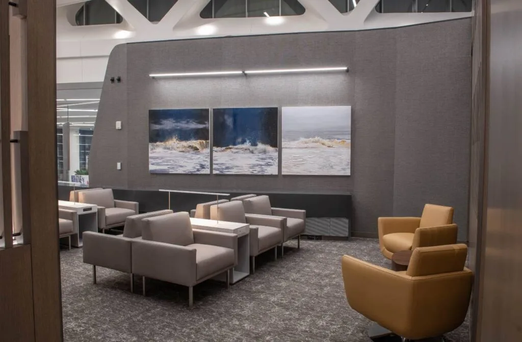 Air Canada lounge seating area with mustard-yellow armchairs, gray lounge chairs, and triptych wave artwork on the wall.