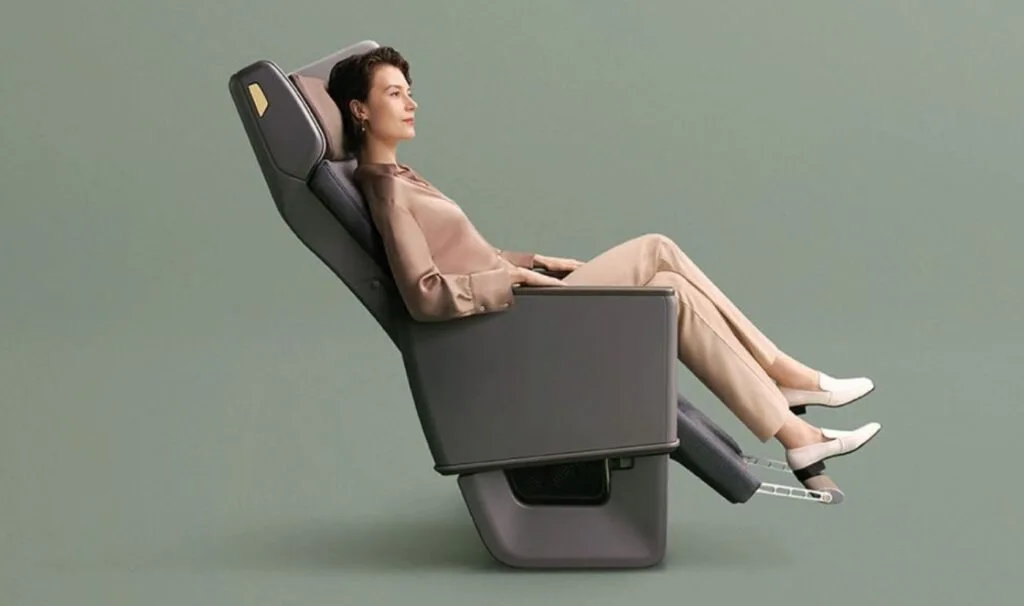 A product photo of a reclined premium economy seat with a footrest extended, modeled against a plain green background.