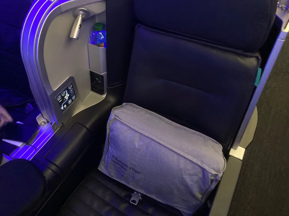 Close-up of a JetBlue Mint suite seat with a gray 'Choose your snooze' pillow and in-seat controls