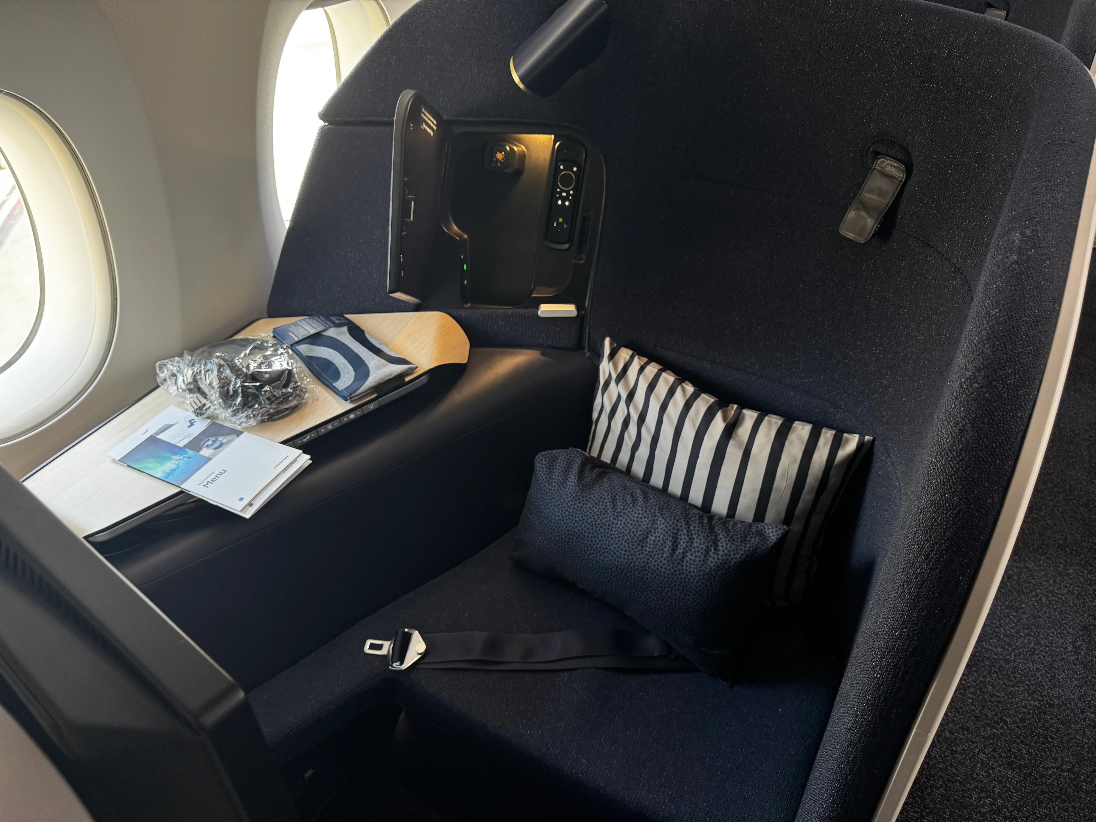 Close-up of a Finnair A350 business class seat with an open entertainment screen, tray table, and pillows, seen from a window-side angle.