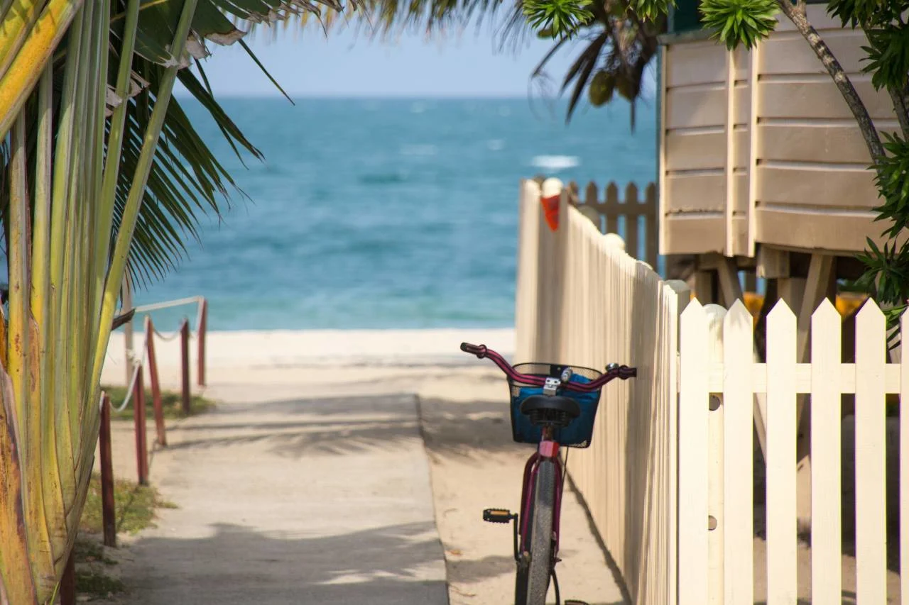 A bicycle parked beside a white picket fence along a sandy path leading to the beach in Key West