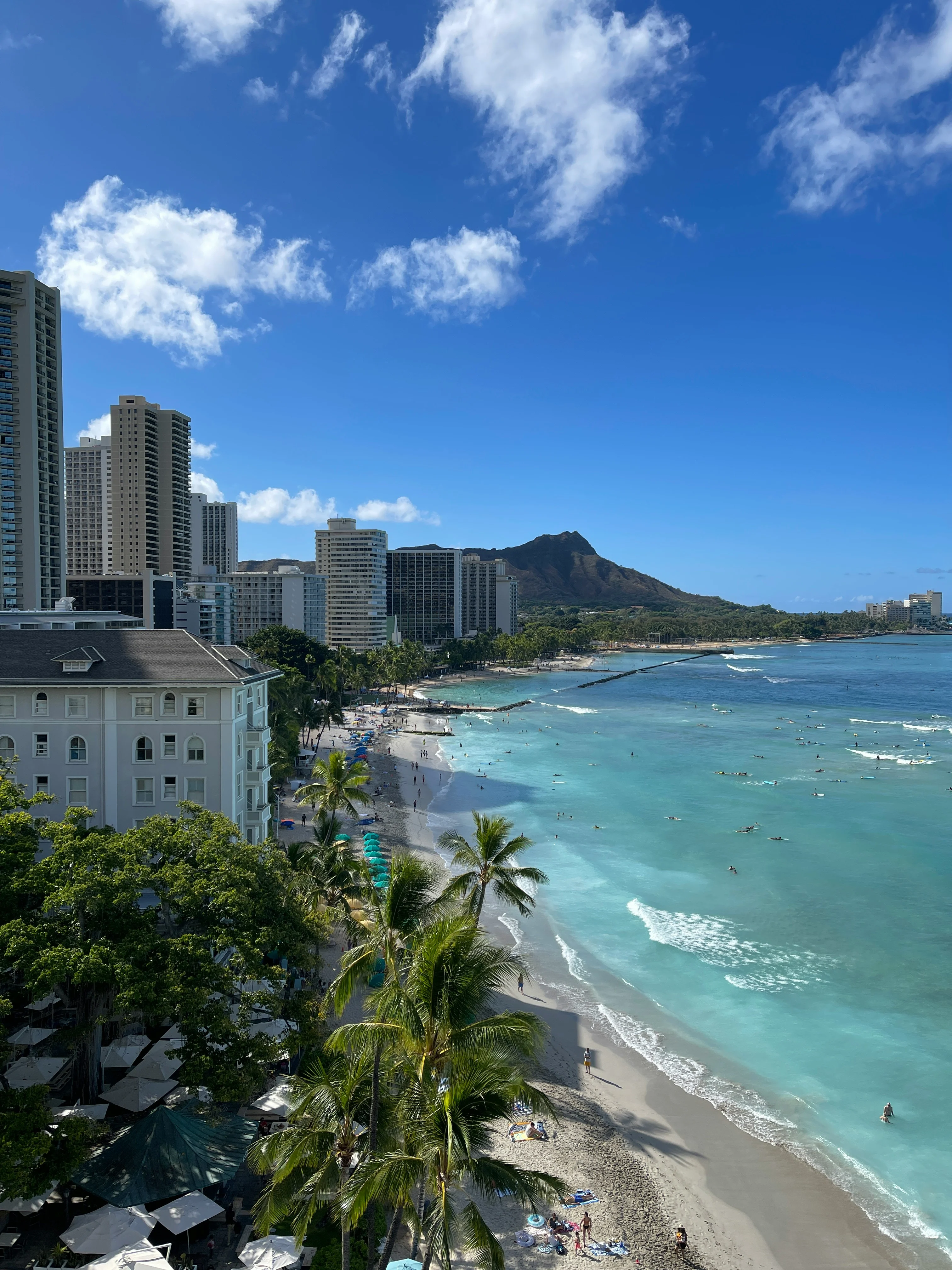 Aerial view of Waikiki Beach in Honolulu with Diamond Head crater in the background, surfers in the water, and beachfront hotels