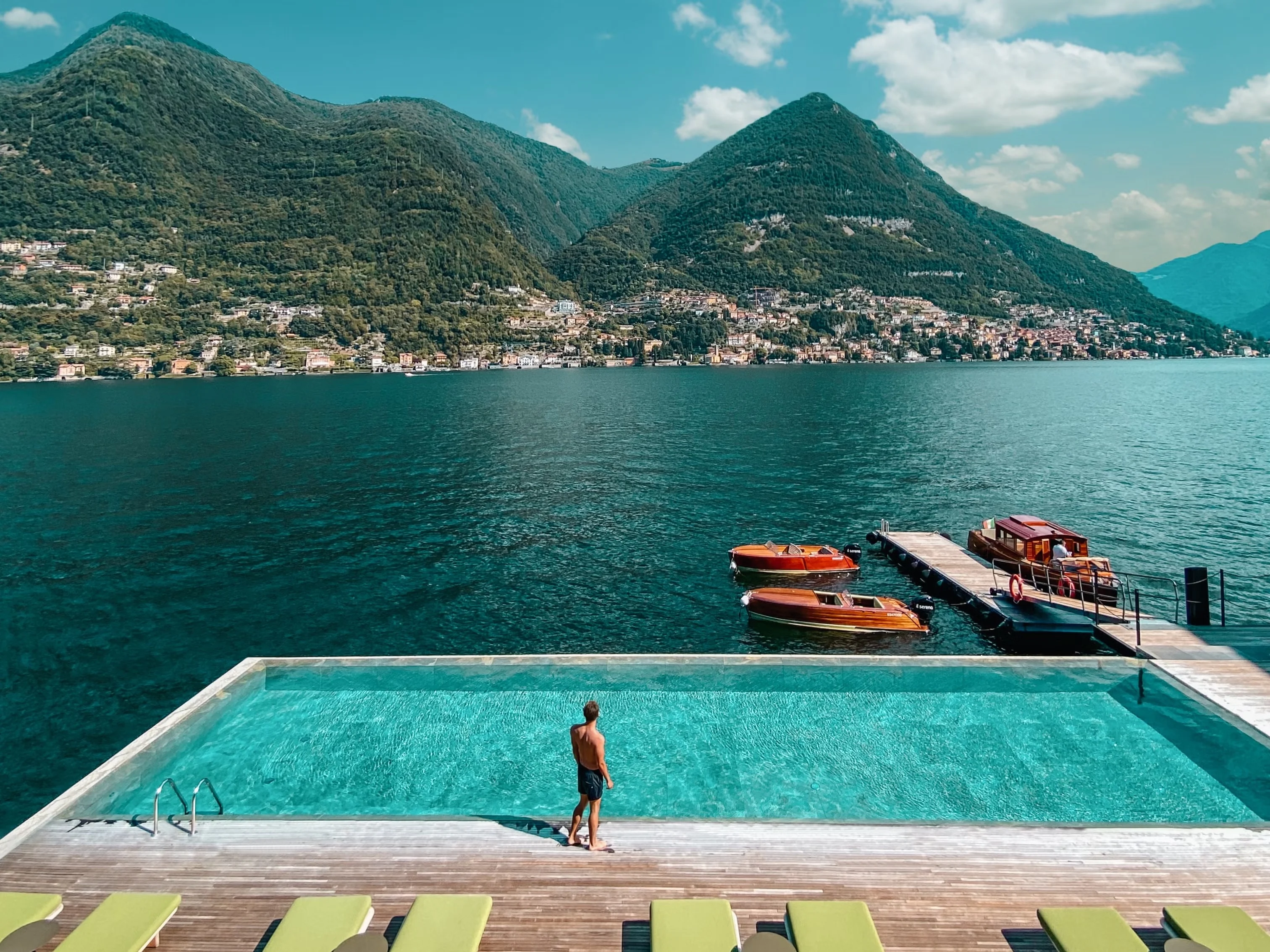 This photo shows towering mountains behind Lake Como with a stunning pool and a male overlooking the beautiful Italy countryside.