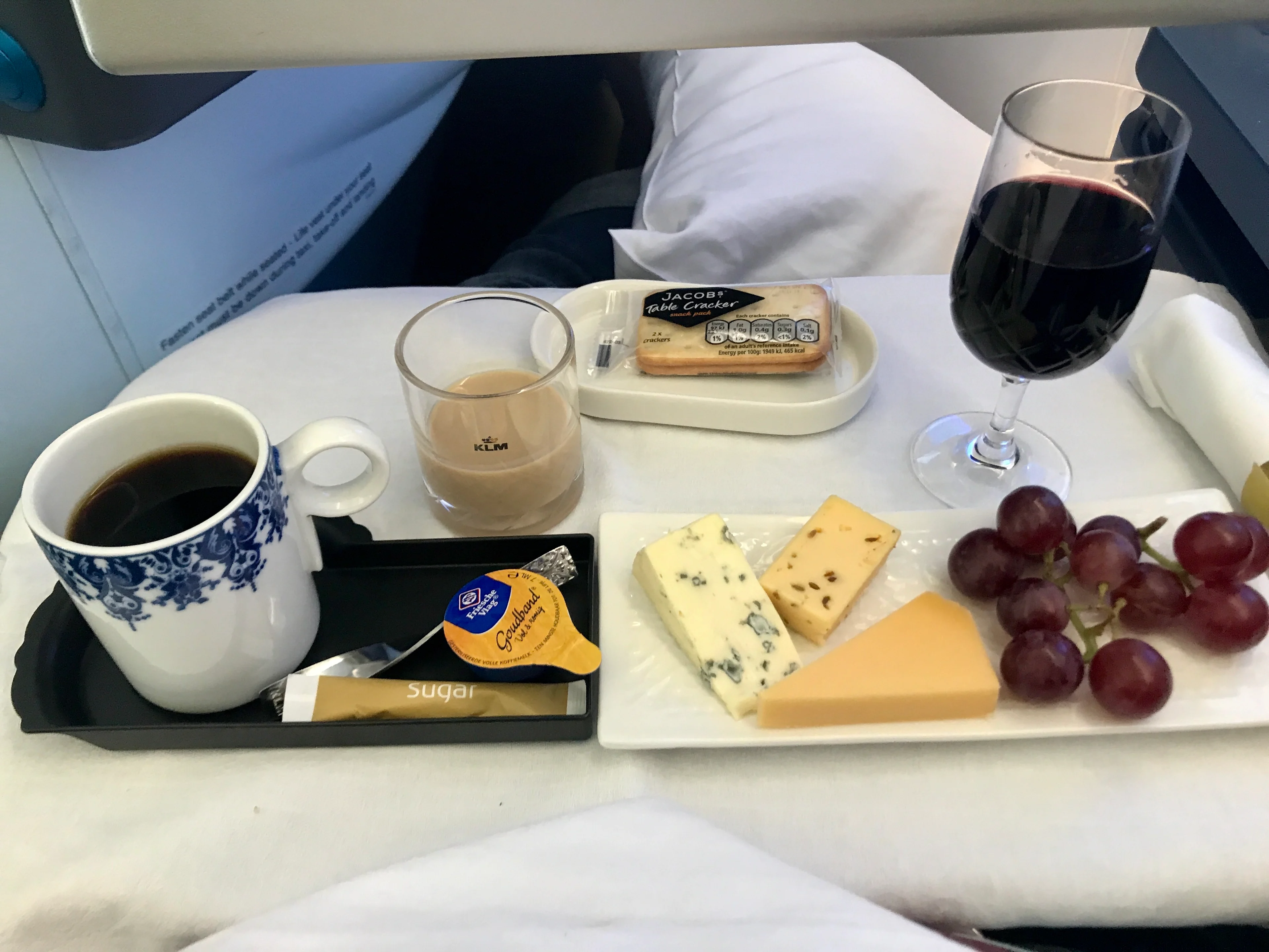 KLM in-flight tray with coffee, tea, wine, crackers, cheese, and grapes served on a business class table