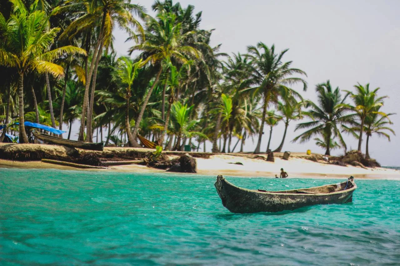 A wooden dugout canoe floats on turquoise water off a palm-lined beach in Panama's San Blas Islands