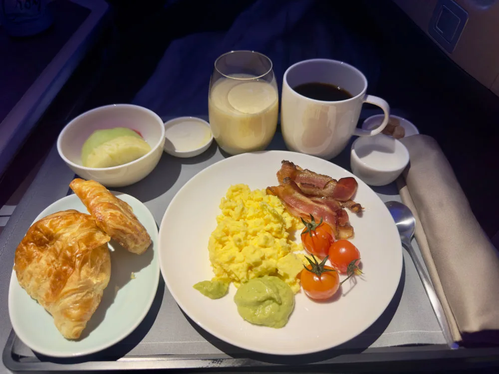 A Cathay Pacific business class breakfast tray with scrambled eggs, bacon, tomatoes, pastries, fruit, coffee, and juice