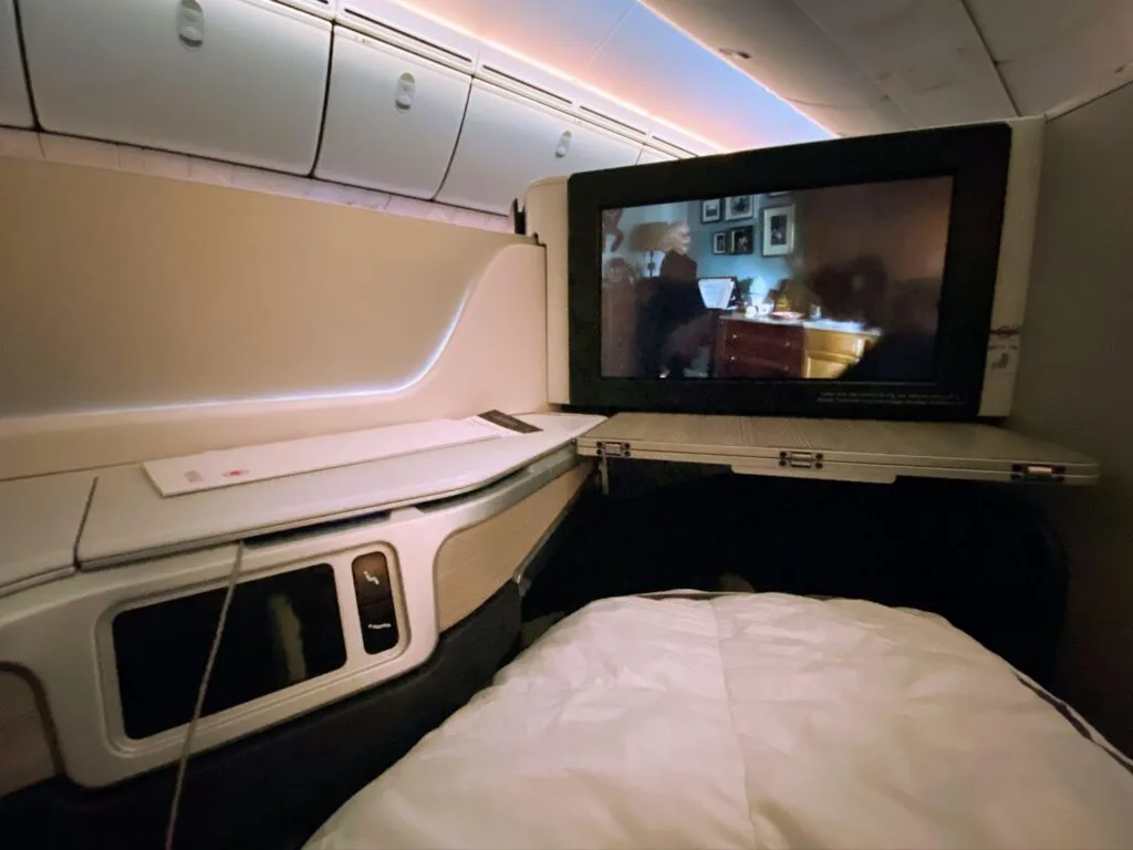 Air Canada business class seat at night with the entertainment screen playing a movie and the tray table extended.