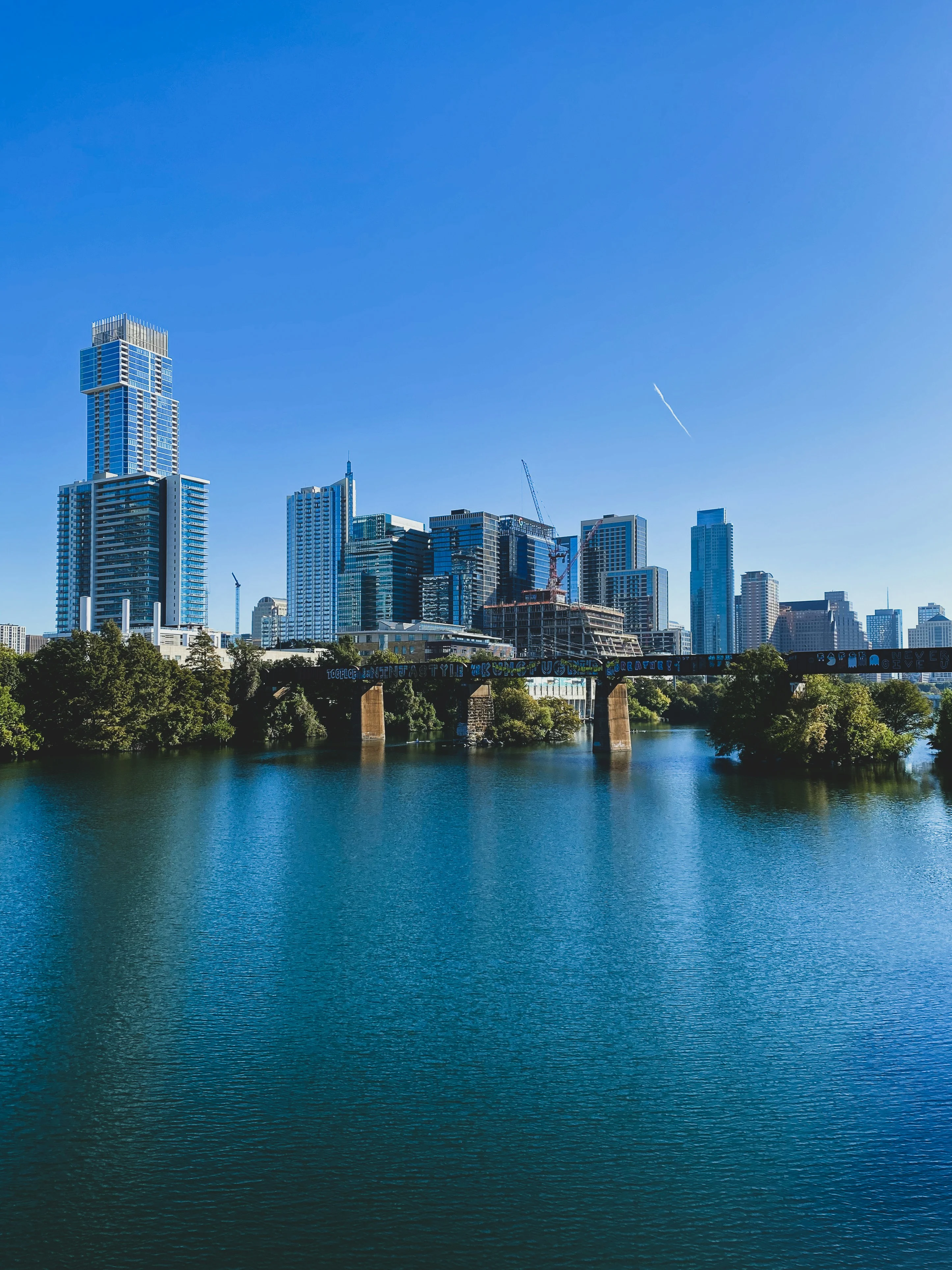 Austin, Texas skyline reflected in a river with a pedestrian bridge and downtown skyscrapers under construction