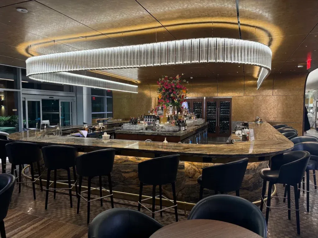 The circular marble bar at the Delta One Lounge in New York JFK, illuminated by an oval ring light fixture and a large floral centerpiece