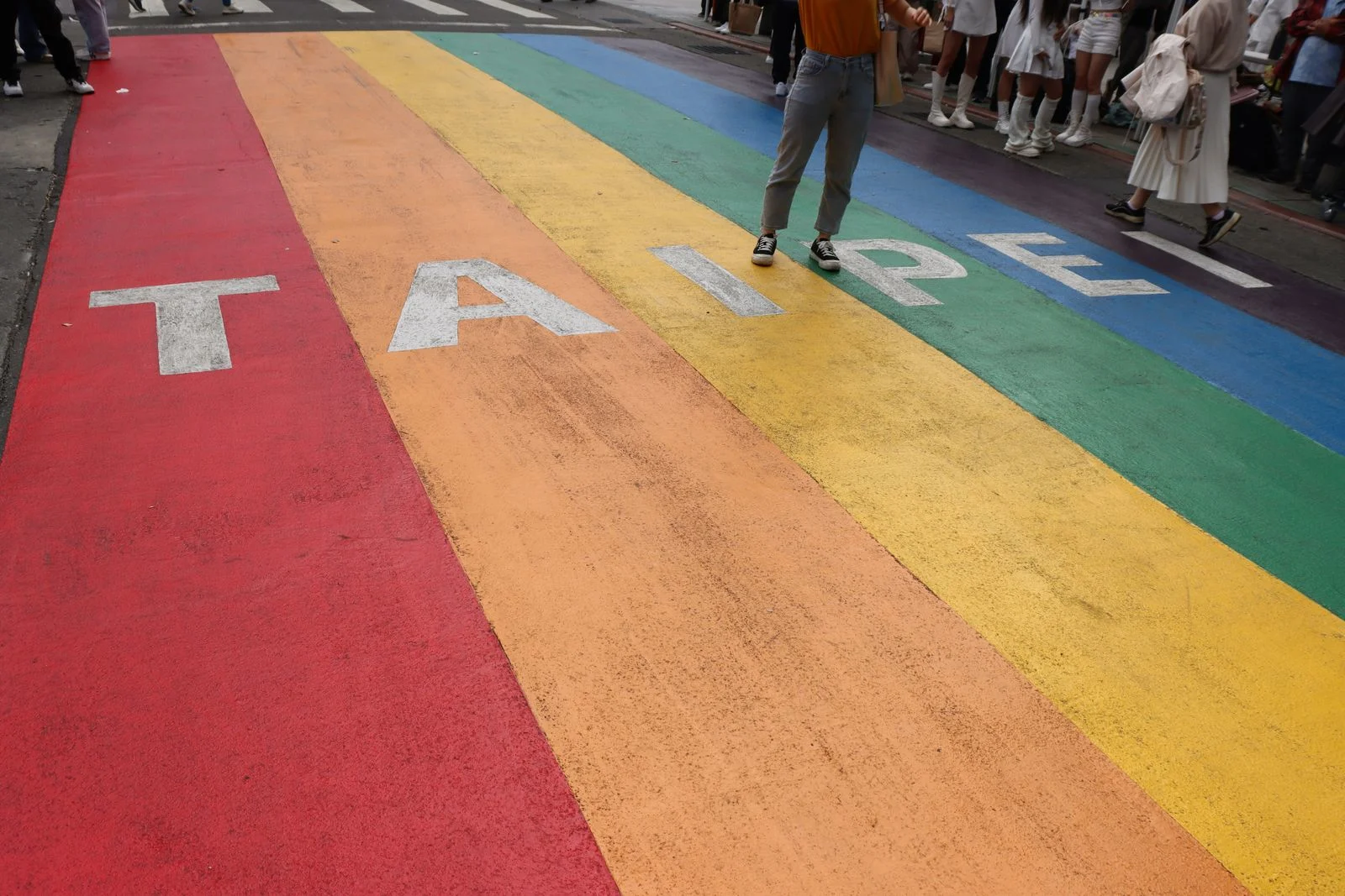 A wide rainbow crosswalk painted with the word TAIPEI marks Pride on a Taipei city street. A wide rainbow crosswalk painted with the word TAIPEI marks Pride on a city street; Taipei hosts the largest Pride parade in Asia.