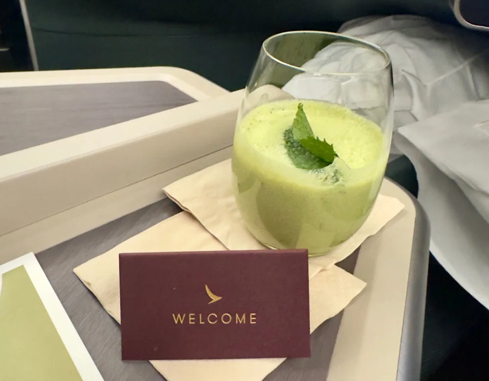 A green welcome drink and a Cathay Pacific business class welcome card on a tray table