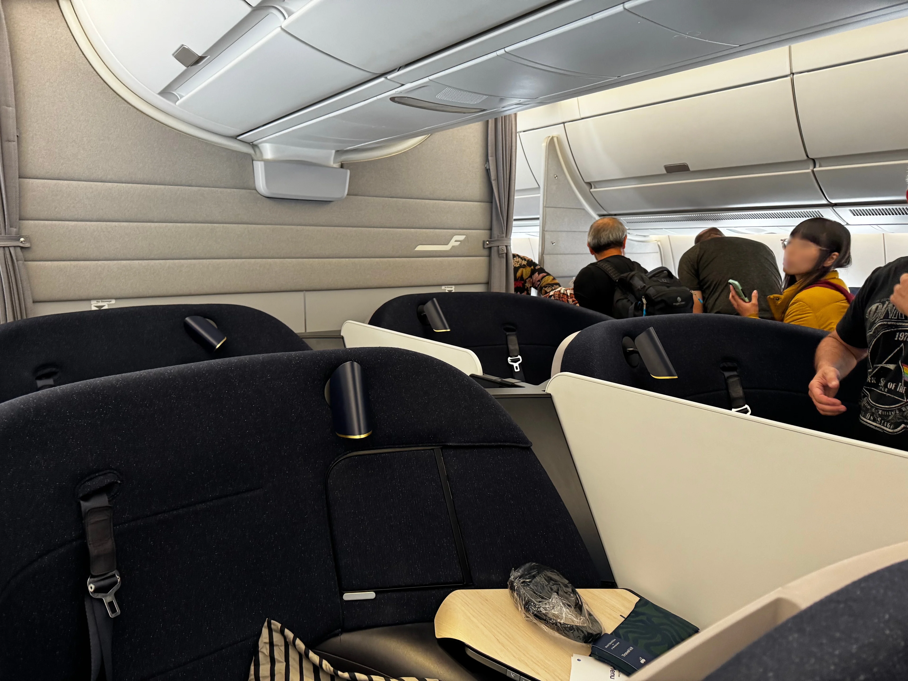 Finnair A350 business class seats in the foreground with passengers boarding and stowing bags near the cabin divider in the background.