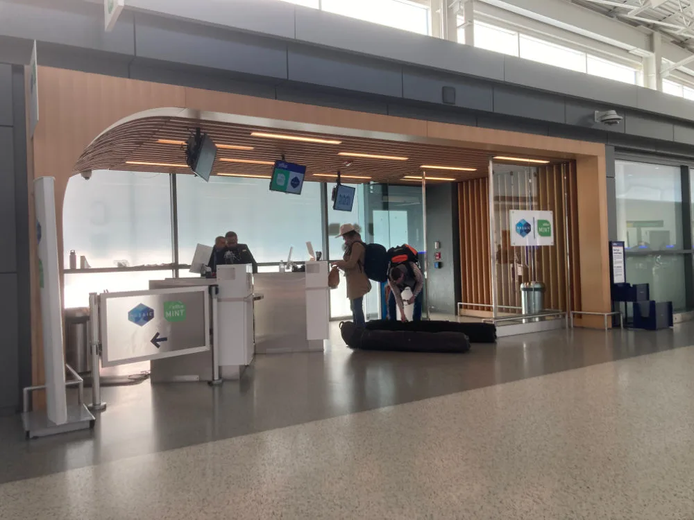 Exterior of the JetBlue Mint check-in area with Mosaic and Mint signage at JFK Terminal 5, with passengers checking bags