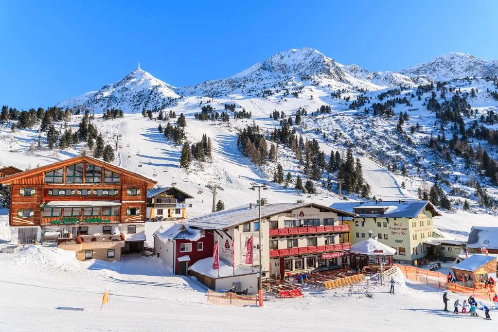 A snow-covered Austrian ski village with traditional wooden chalets and a ski slope rising toward the surrounding mountains