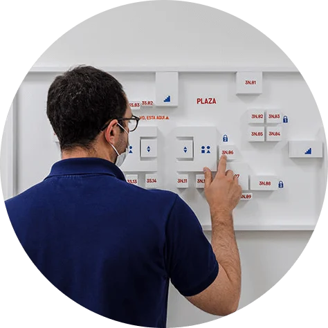 A man in a dark blue shirt faces and points at a white board with several white 3D models on it.