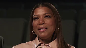 A Black woman with long brown hair. She wears a pink jacket.