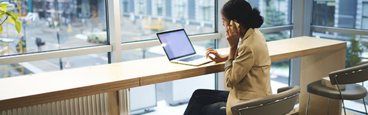 Woman in front of large windows working on laptop