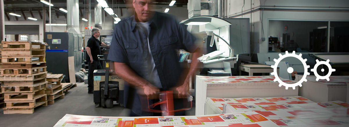A man pushing pallet of printed output in print shop overlayed with gear icons