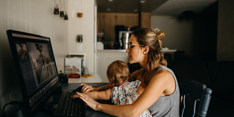 Woman working at desk on her computer in her house with child on her lap. 