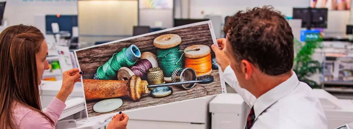 two people examining a print sample of cotton reels near a Xerox digital press