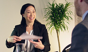 Smiling woman handing papers to someone offscreen