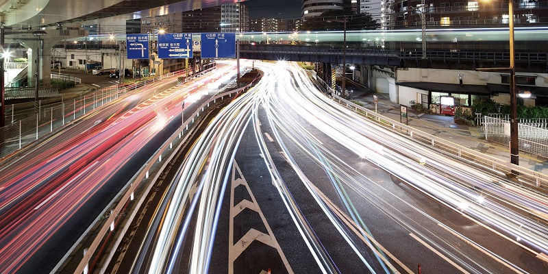 Photo of a highway underpass at night with streaking car headlights and taillights